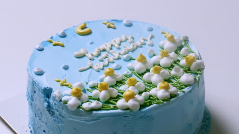 round cake with blue-colored icing and a happy birthday text written in white icing and decorative flowers made of icing