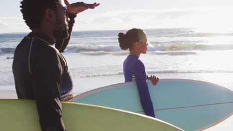 african american couple carrying surfboards on the beach