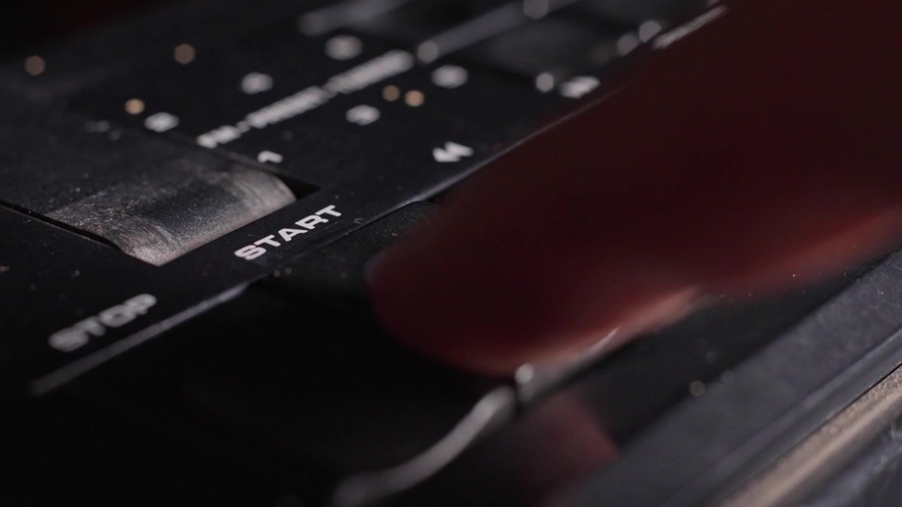 Close detail of vintage analog audio controls with black start and stop buttons on analog equipment, finger presses down play button