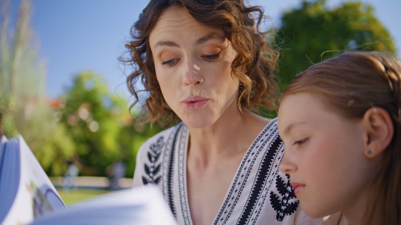 Young mom reading book toddler girl resting together at weekend garden closeup