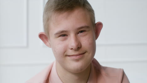 Close-up-view-of-a-boy-with-down-syndrome-smiling-at-camera-sitting-on-the-bed-in-the-bedroom-at-home