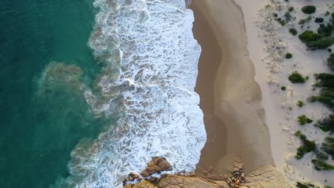 top-down shot of foamy wave splashing on the sand at the beautiful paradise in knight beach, port elliot, australia - aerial slow motion