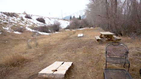 Empty-cornhole-game-in-a-snowy-park-during-the-day-with-mountains-in-the-background,-handheld