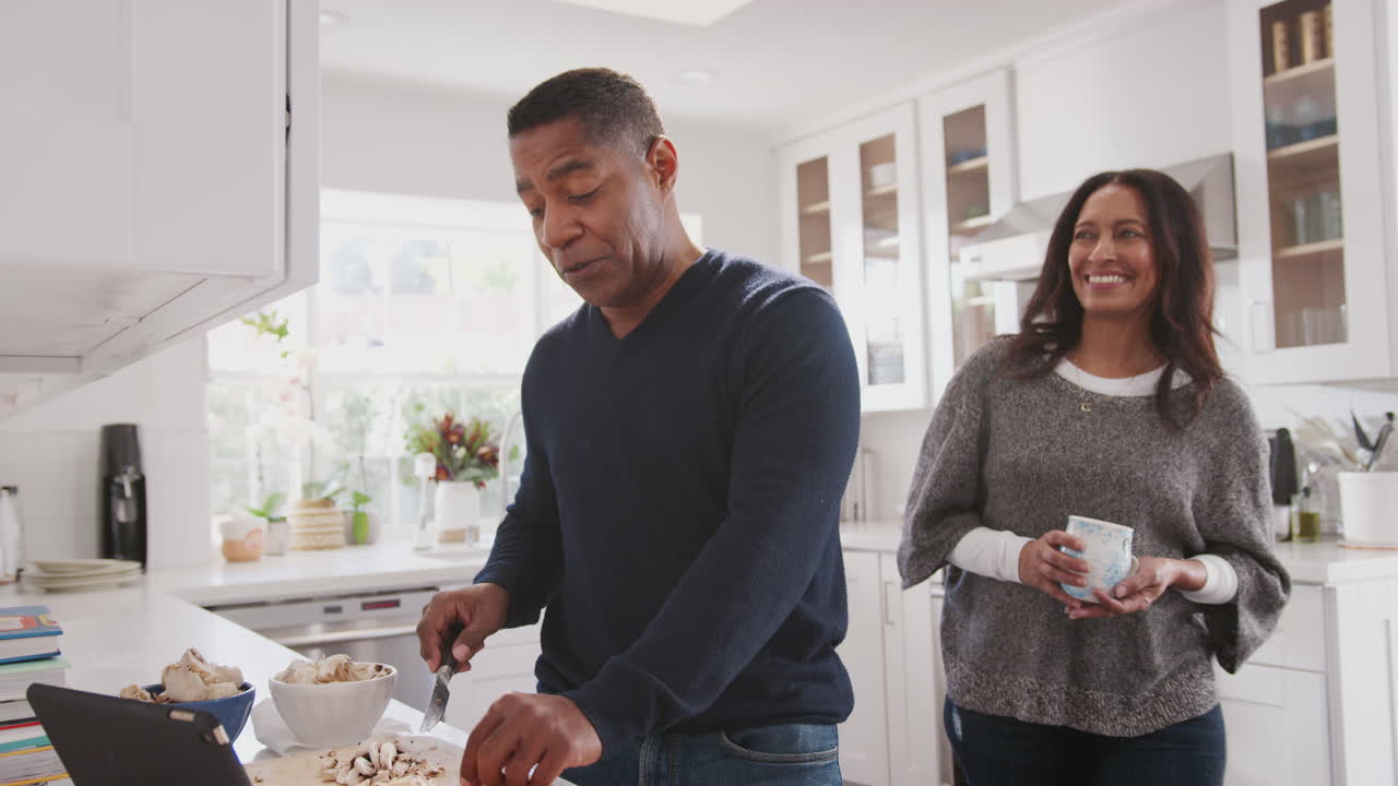 Middle aged man preparing food in the kitchen, his partner standing with him talking