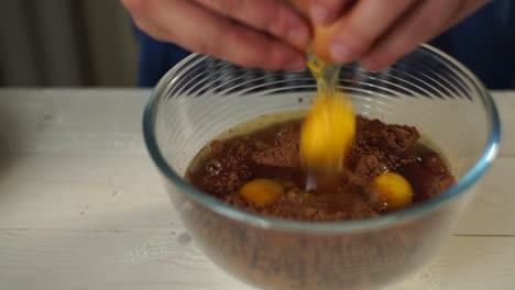 las manos del chef rompiendo el huevo y añadiendo en un cuenco de vidrio. preparando pastel casero