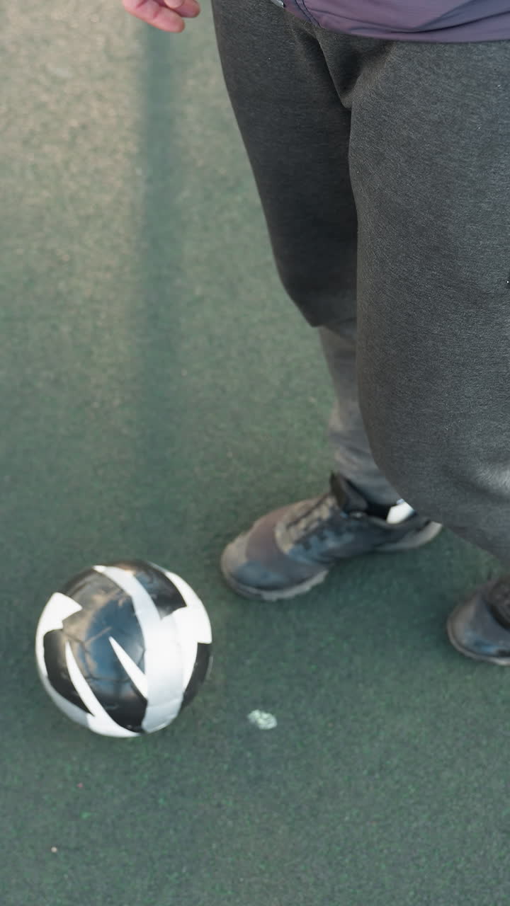 vista aérea de un atleta que demuestra movimientos precisos del tobillo con una pelota de fútbol en el suelo, centrándose en la agilidad y el control durante una sesión de entrenamiento en una superficie deportiva texturizada en un entorno al aire libre