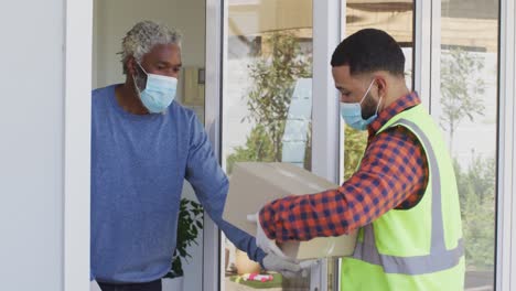 delivery man delivering package to senior man wearing face mask at home