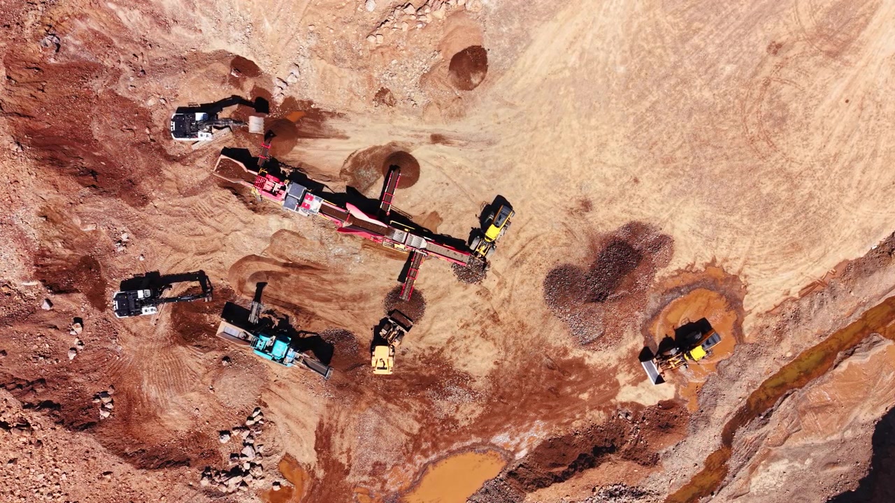 Overhead view of multiple hydraulic diggers working around a mobile sorting screener on rocky excavation ground. Excavators and crushing machinery inside stone quarry.