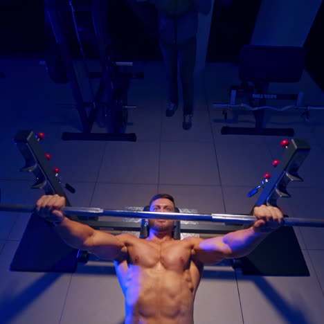 bodybuilder trainer man doing bench press workout in gym. video from the top. blue light filter. naked torso. strong abs.