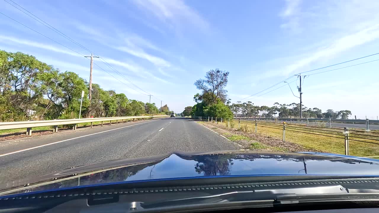A car travels through Geelong's rural roads under clear blue skies, capturing the serene landscape and natural beauty