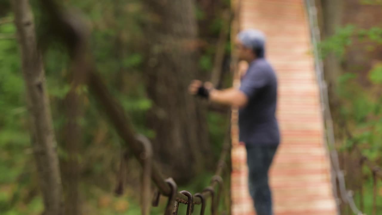 hombre caminando sobre un puente colgante de madera en un bosque