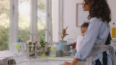 Madre-Feliz-Sosteniendo-Al-Bebé-En-Casa-Mamá-Cansada-Tomando-Café-Relajándose-Después-De-Las-Tareas-Domésticas-Lavando-Platos-En-La-Cocina