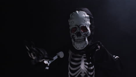 fotografía de estudio de un niño vestido con un disfraz de esqueleto haciendo un truco o un regalo en halloween bailando rodeado de humo contra un fondo negro