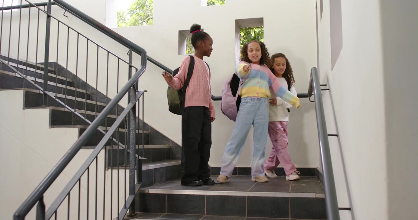 African American students going down stairwell holding rail wearing backpacks pointing at windows