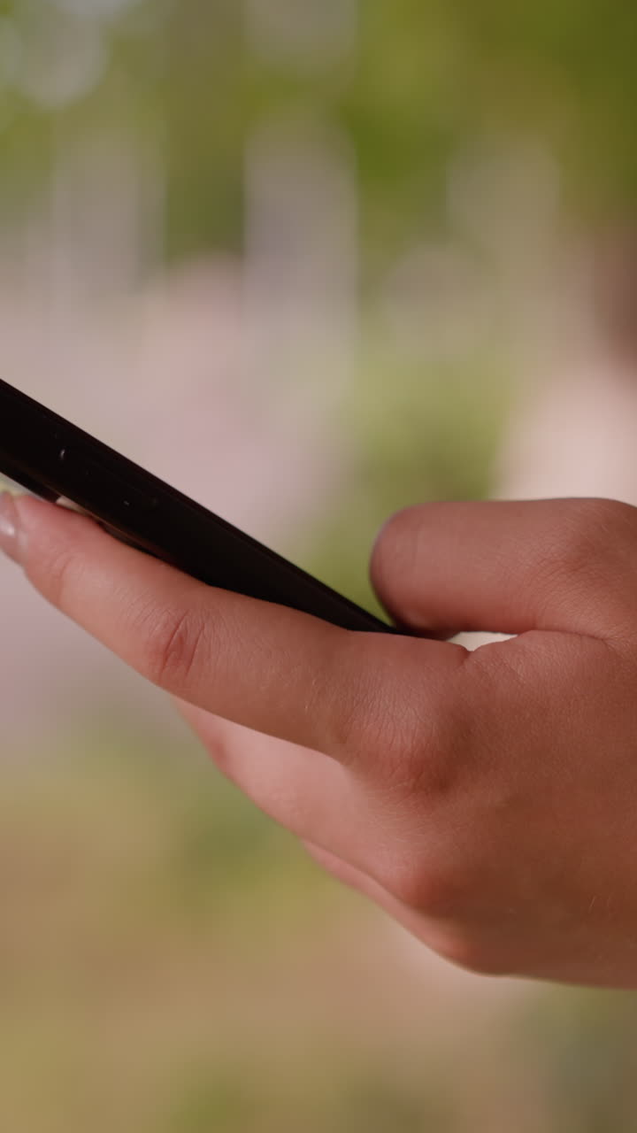 primer plano de un teléfono inteligente individual que opera a mano con enfoque en las manos, fondo natural borroso con vegetación y figura poco clara en la distancia