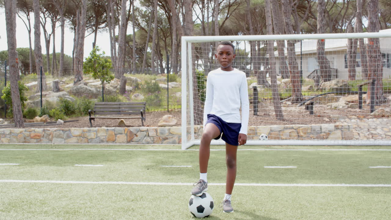 Menino afro-americano jogando futebol no campo, em pé com a bola com confiança, espaço para texto