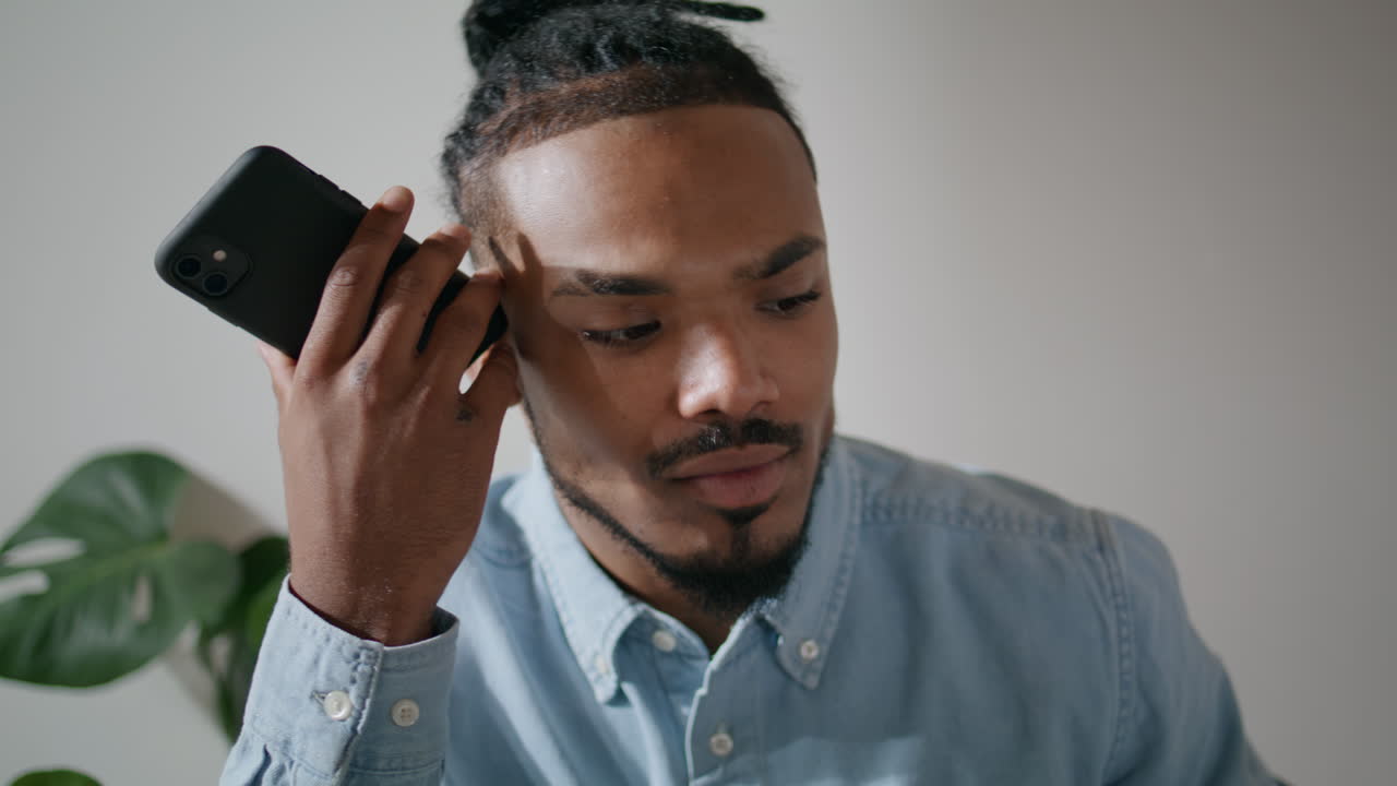 Dreadlocks guy listening message at loft office closeup. Man holding smartphone