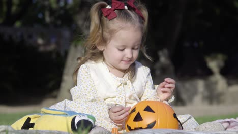 Cerca-De-Una-Adorable-Niña-Sentada-En-La-Manta-Y-Jugando-Con-La-Calabaza-De-Halloween-En-El-Parque-De-La-Ciudad