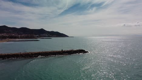 Costa-De-Sitges-Con-Mar-Resplandeciente-Y-Horizonte-Montañoso-En-Un-Día-Soleado,-Vista-Aérea