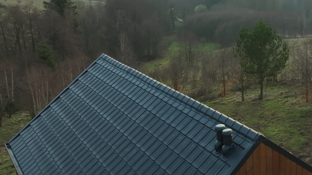 vista cercana de un techo inclinado con azulejos grises en una casa de madera, rodeada por un paisaje de hierba con árboles escaros