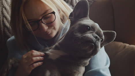 close up view of red haired woman caresses her bulldog dog while they are sitting on the sofa in the living room at home 5