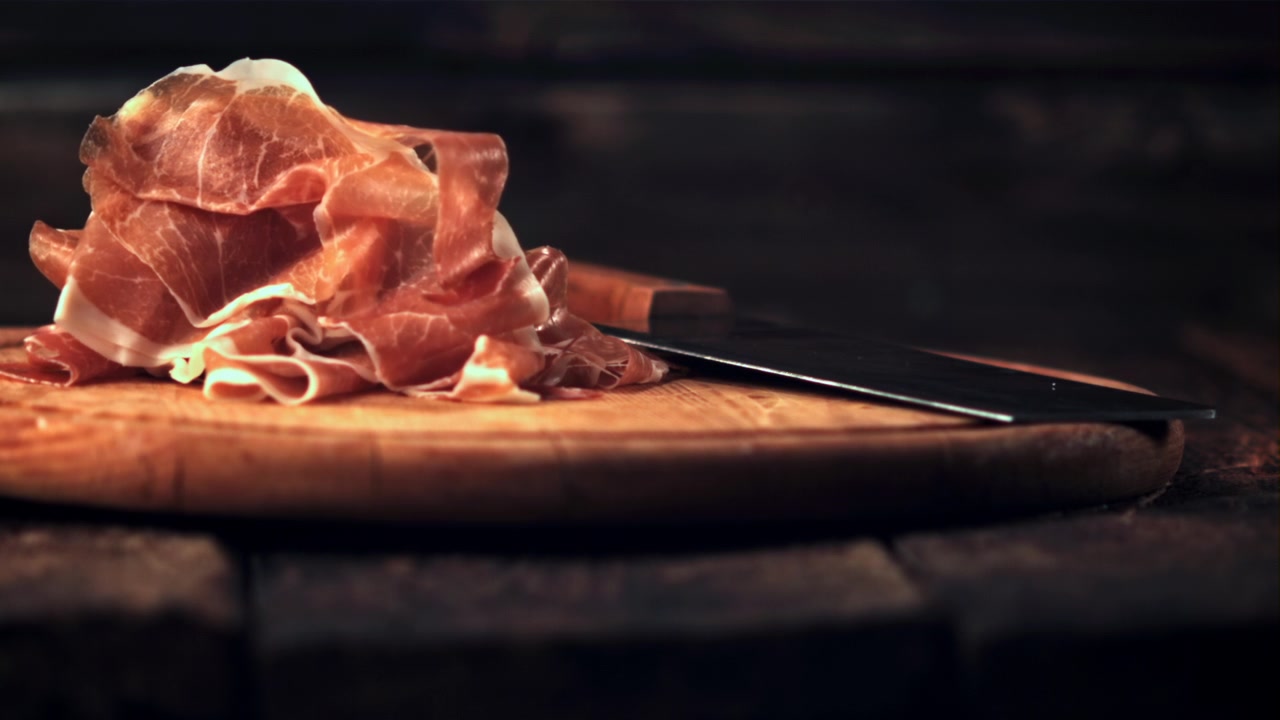 Fette di prosciutto che cadono al rallentatore su un tagliere di legno