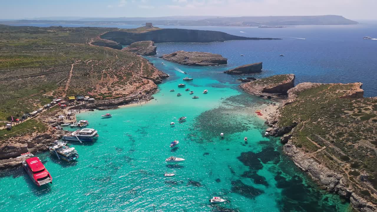 Blue Lagoon, Comino, Malta, con l'isola di Cominotto, è caratterizzata da acque cristalline turchesi, costa rocciosa, barche e nuotatori in questa baia mediterranea, catturata da una prospettiva aerea.