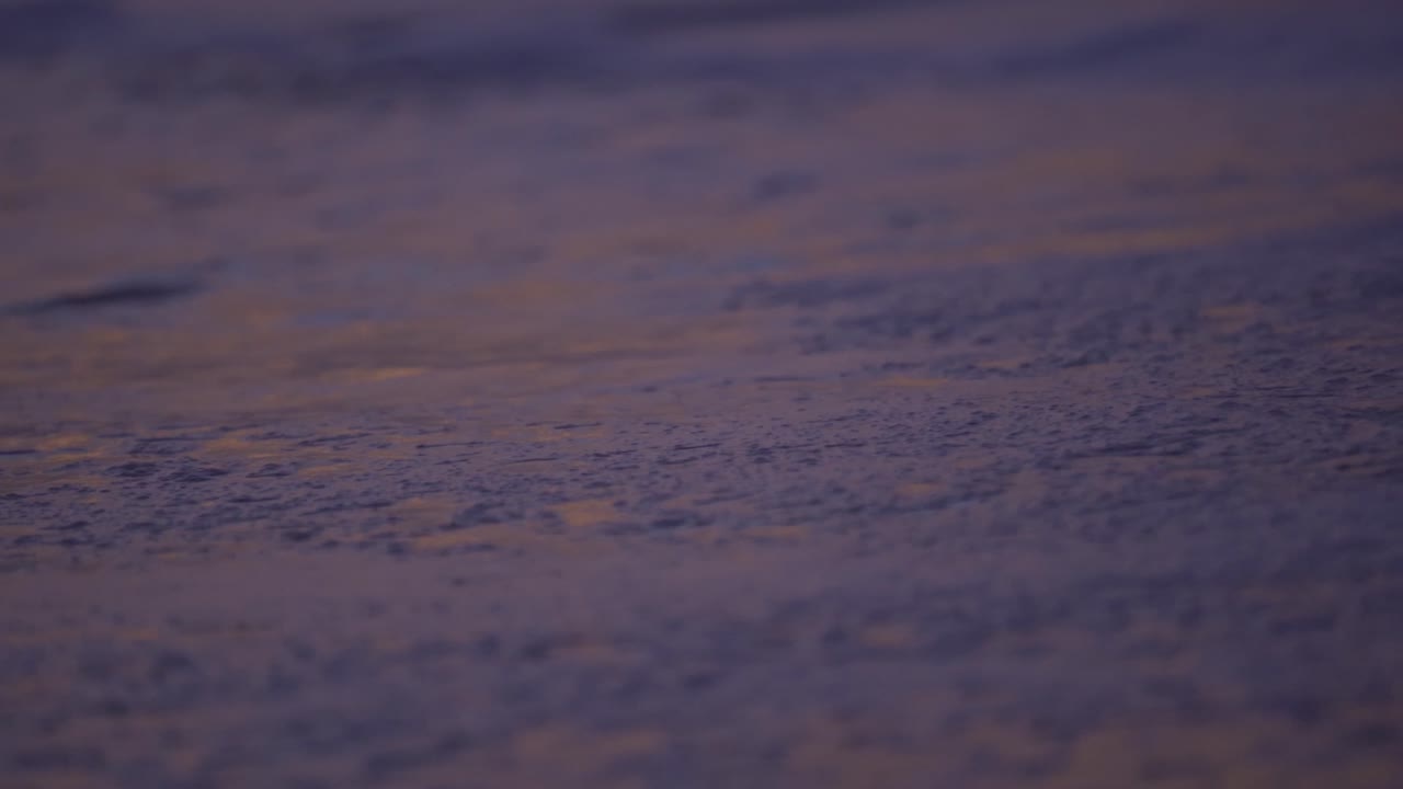 A close-up, abstract shot of the ocean's surface during twilight, painted in soft, serene hues of purple and magenta