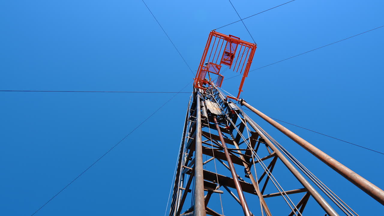 Standing under the drilling derrick for producing oil or gas. Low angle view at the tower with guyed mast on top.
