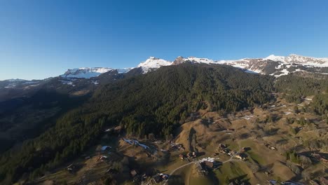 Snow-covered-peaks-behind-green-hilltops-and-village-in-valley