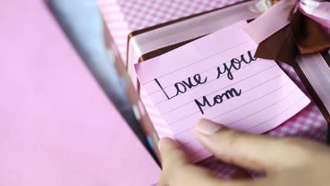 hand holding a note that says "love you mom" on a gift box