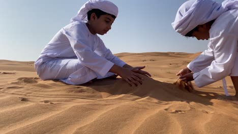 two emarati children playing with sand in the desert