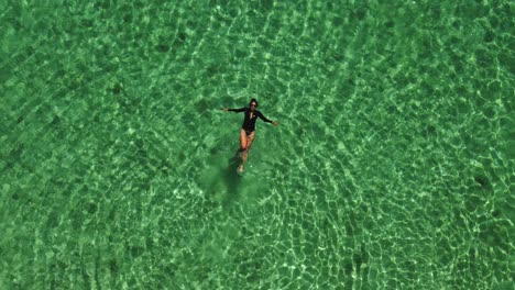 aerial view: woman in black swims in bright green water, copy space