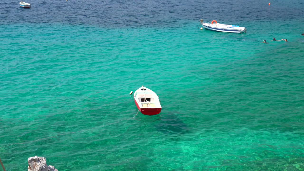 barco de madera blanca y roja flotando en agua de mar turquesa, peloponeso