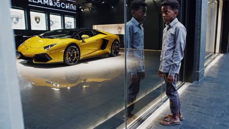 young boy standing on the sidewalk, gazing at a stunning yellow supercar parked inside a luxury car dealership, envisioning a future filled with ambition and success