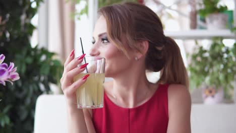 young woman with long blonde hair sitting at the table and relaxing in the cafe and drinking tasty lemonade. slow motion shot