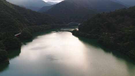 picturesque view of a serene river surrounded by lush mountains with suspension bridge in okutama lake, japan