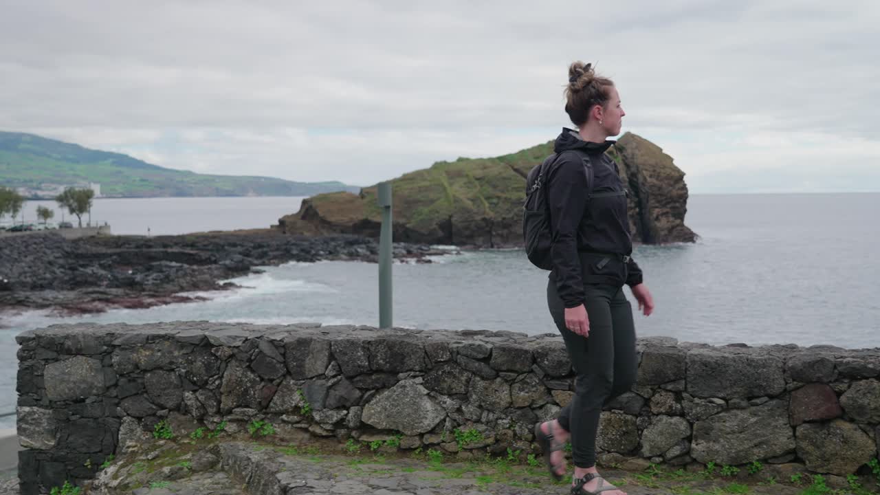 Woman close to the waters edge near a rocky shore in Ponta Delgada, Azores, Portugal