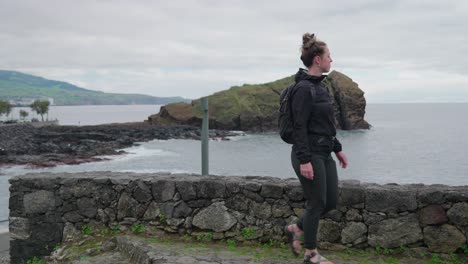 Woman-close-to-the-waters-edge-near-a-rocky-shore-in-Ponta-Delgada,-Azores,-Portugal