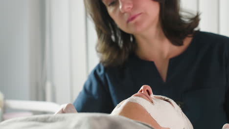 bodywork therapist applies gentle face scrub using soft silicone brush on client skin during relaxing spa treatment under bright studio light highlighting professional skill and calm atmosphere