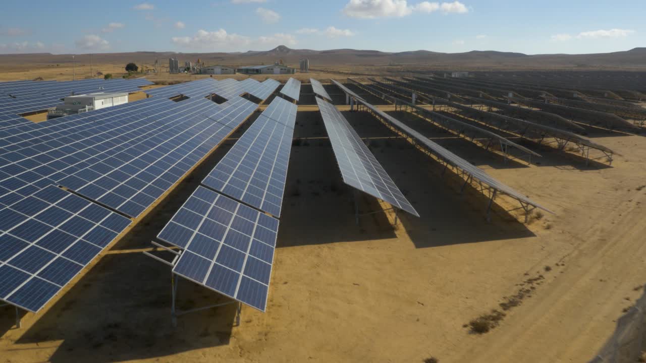 toma aérea de drones: entrar en un campo cercado con muchos conjuntos de paneles solares tirados en la tierra en medio de un desierto