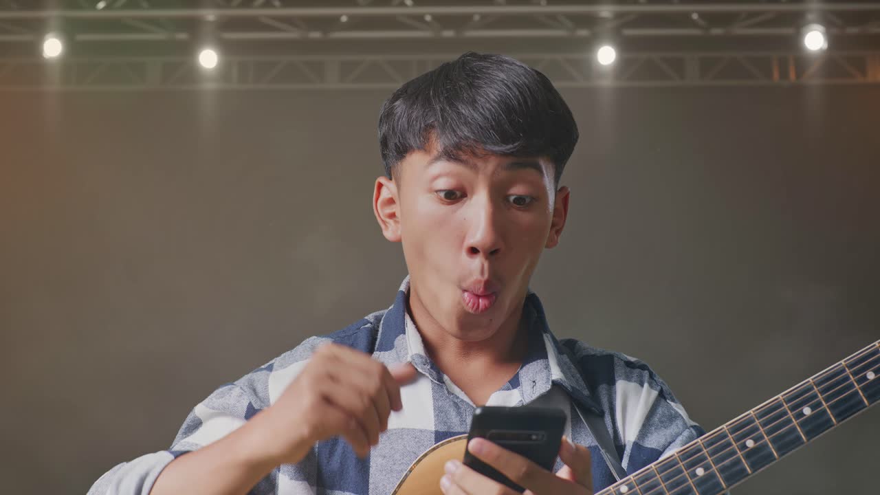 스마트폰을 사용하고 무대에 서서 와우라고 말하는 기타를 들고 있는 아시아 십대의 클로즈업