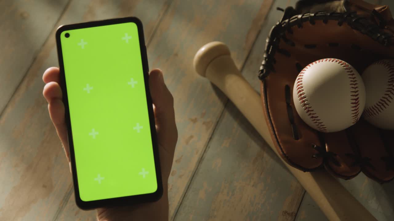 persona con pantalla verde teléfono móvil por encima del béisbol todavía vida con pelota de murciélago y receptores guante en el suelo de madera envejecido 1