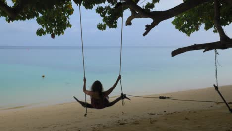 a woman swings on a log on a tropical beach