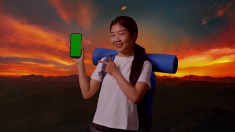 배을 가진 젊은 여성은 산 위에서 해가 뜨거나 해가 지면 초록색 화면 전화를 표시합니다.