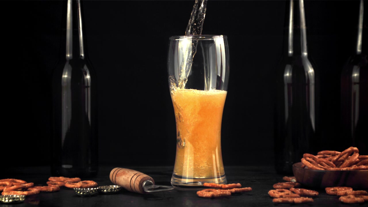 Versamento di birra al rallentatore in un bicchiere con pretzel