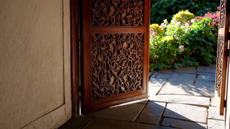 ornately carved wooden door opens to a beautiful garden