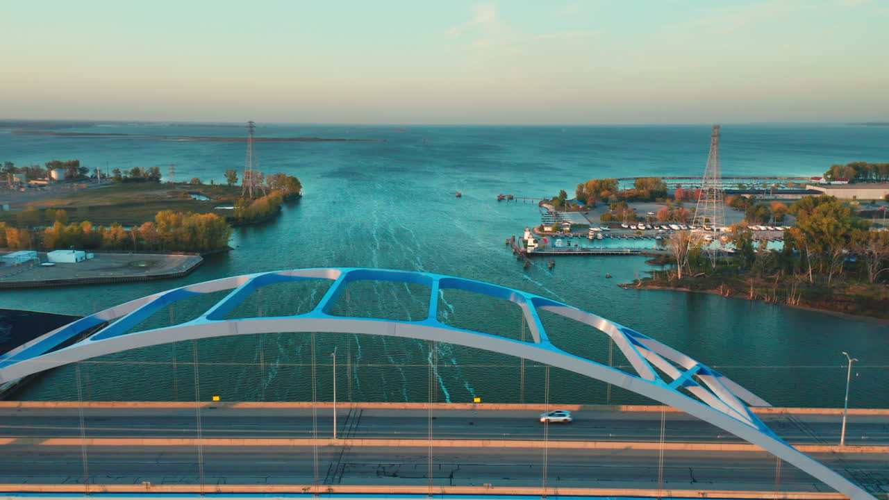 The Leo Frigo Bridge stretches gracefully over calm river waters, its blue steel arch framing boats and shoreline in the distance beneath a bright and tranquil sky