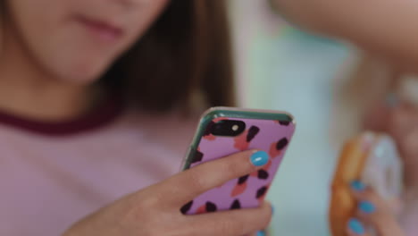 close up beautiful teenage girl using smartphone browsing social media texting friends hanging out eating donuts