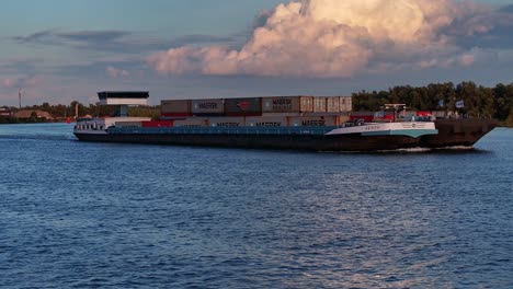 cargo ship sailing on dutch rivers carrying containers of goods at sunset